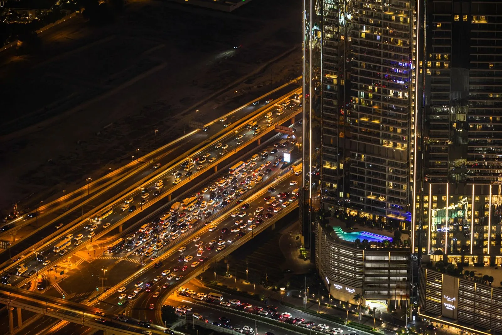 A bustling nighttime cityscape with vibrant traffic and illuminated skyscrapers from above.