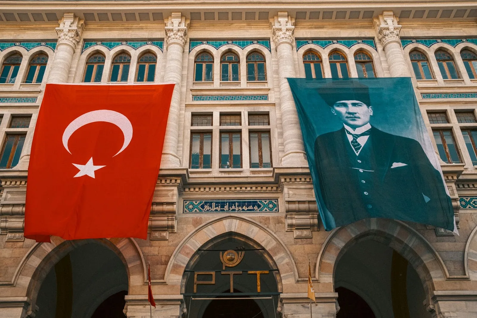 The front facade of Istanbul's PTT Museum with Turkish flag and Atatürk portrait, showcasing Ottoman architecture.