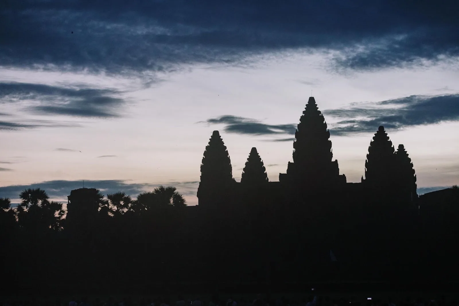 Silhouette of Angkor Wat temple at dusk with dramatic sky.