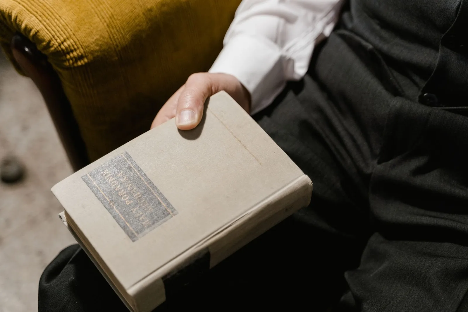Close-up of a hand holding a vintage hardcover book, person in formal attire.