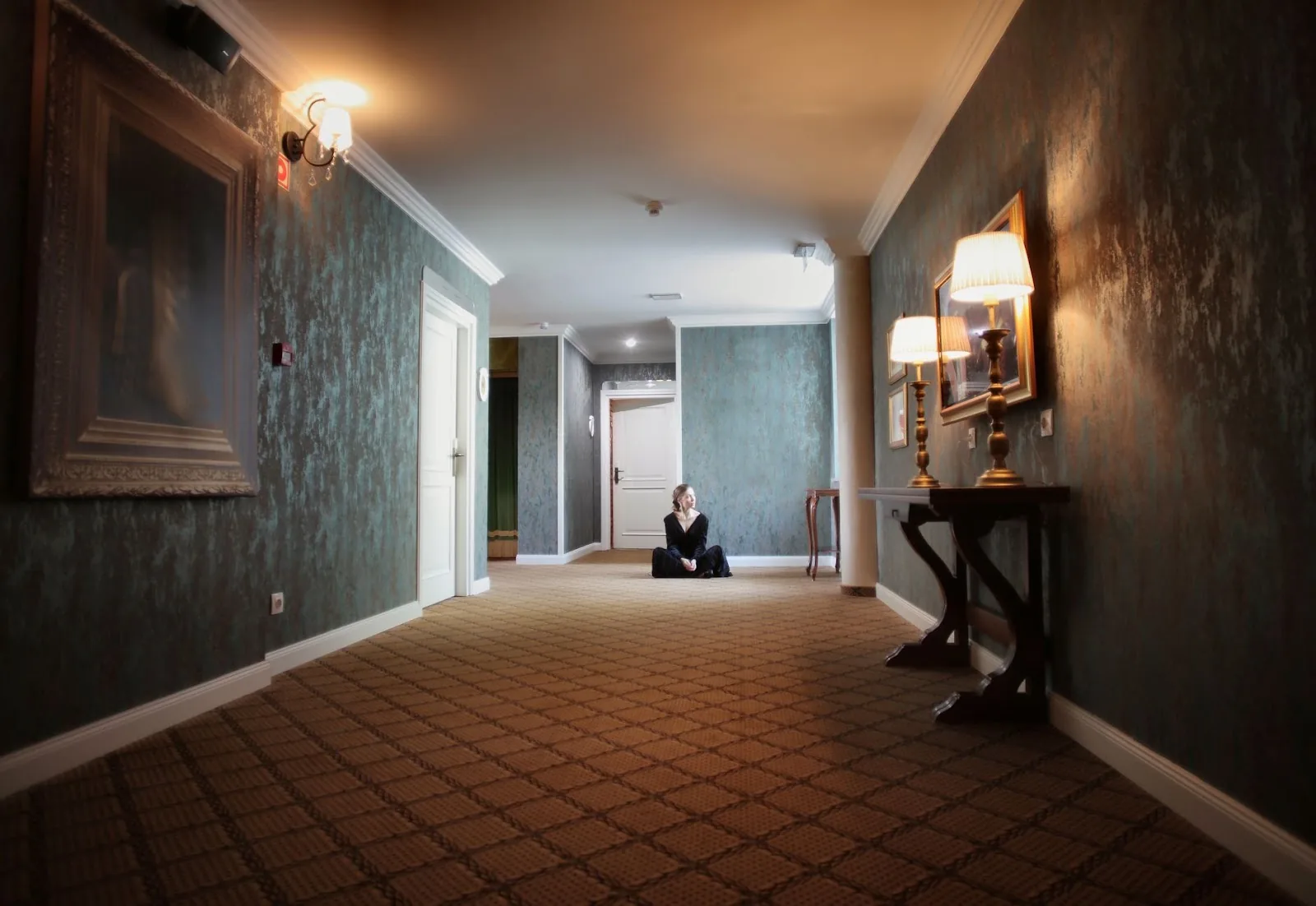 A woman sits peacefully in a luxurious hallway with elegant lamps and decor.
