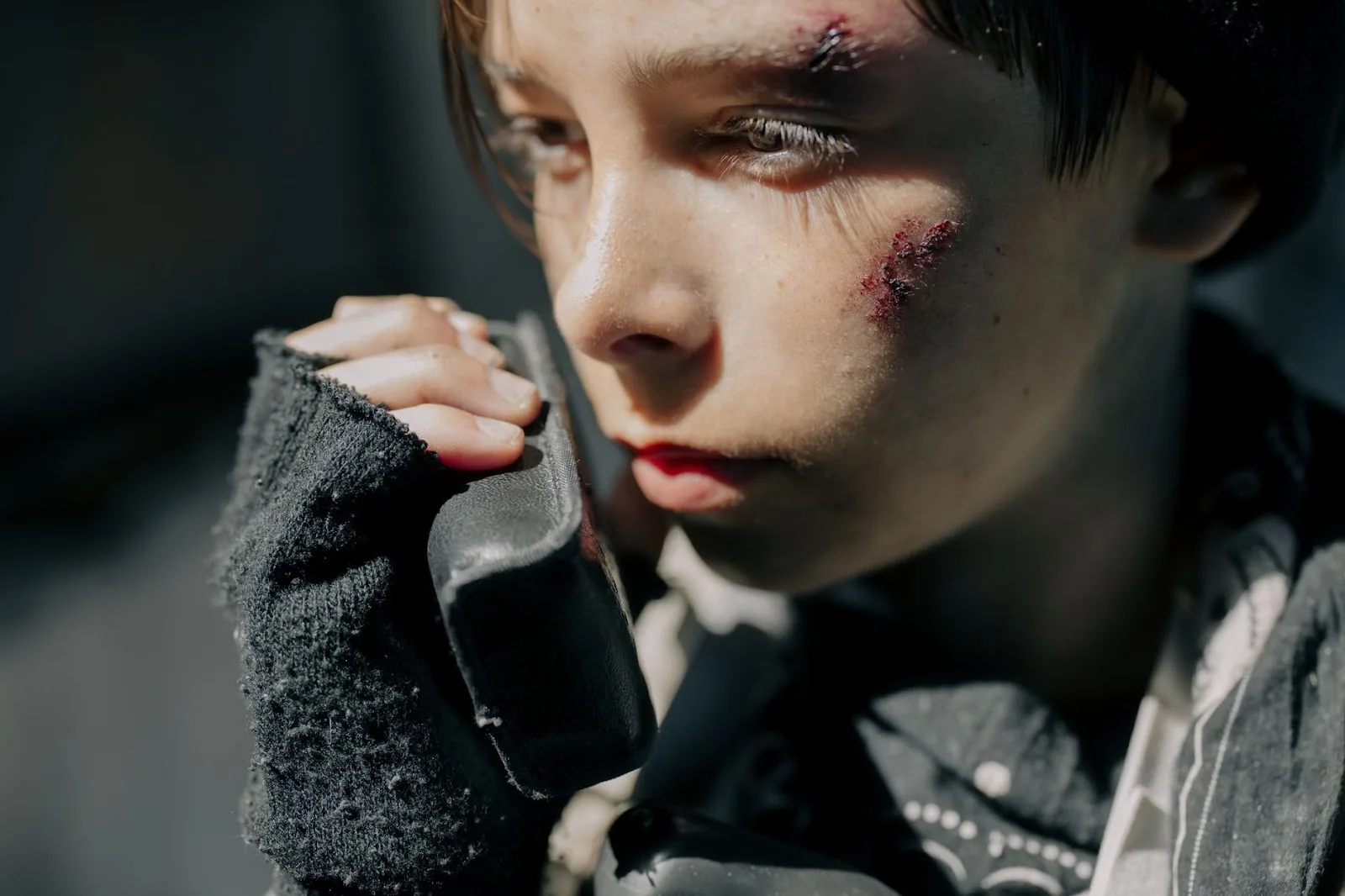 Close-up portrait of a young boy with wounds, using a radio, conveying a survival theme in a post-apocalyptic setting.