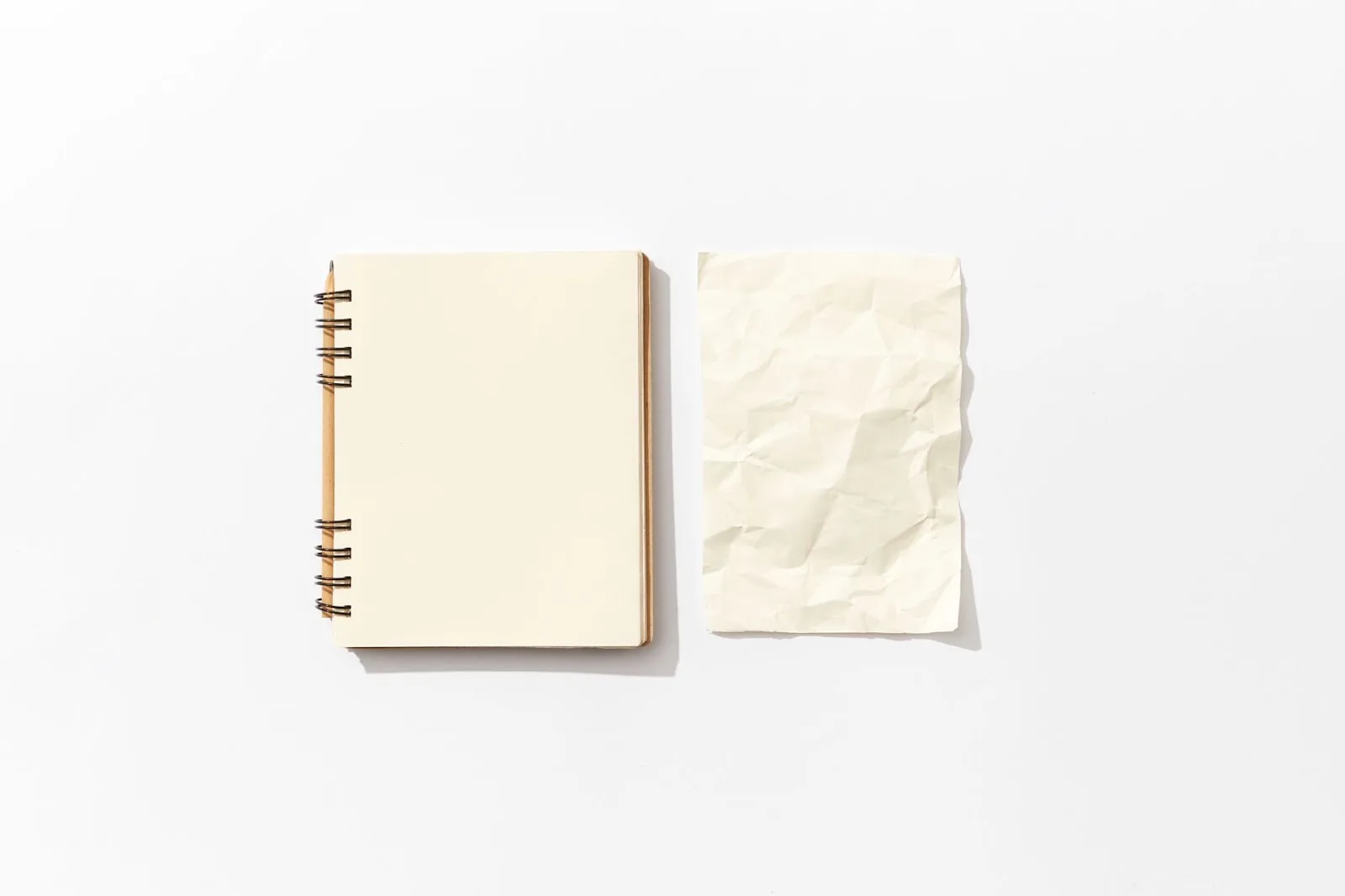 Flat lay of an open spiral notebook and a crumpled paper on a white background, perfect for mockup designs.
